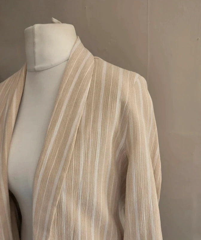 A beige and off-white vertically striped lightweight jacket draped on a white mannequin torso against a neutral gray wall.