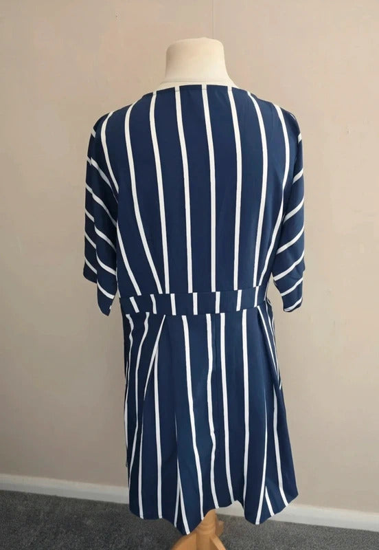 A navy blue and white vertically striped short-sleeve dress displayed on a mannequin from the back, set against a plain beige wall.