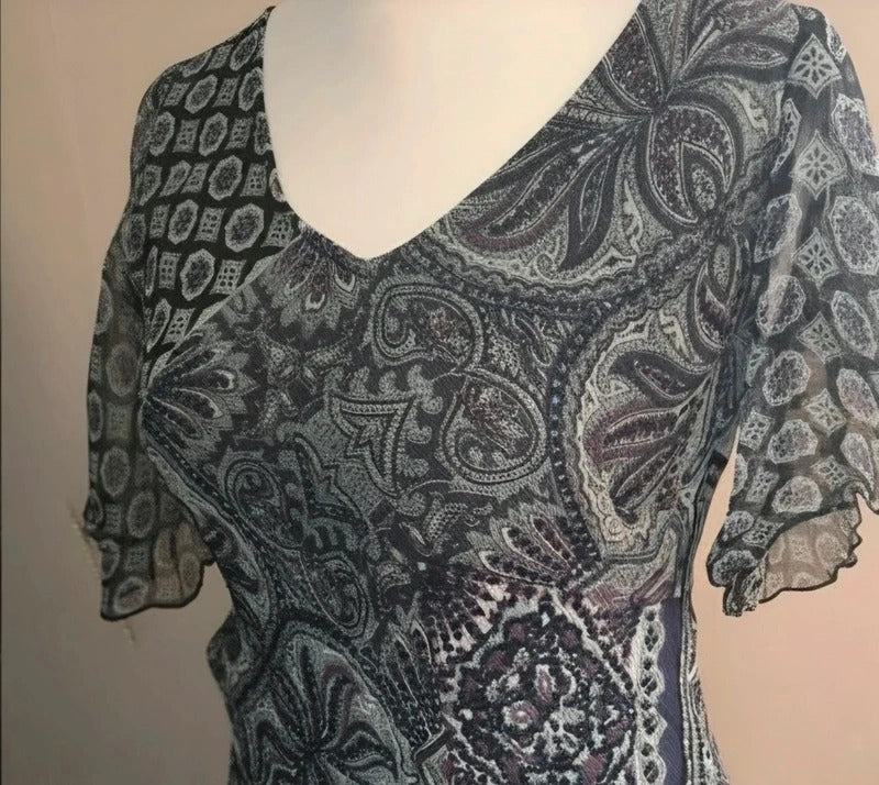 A short-sleeve V-neck dress with a black, gray, and white paisley pattern, displayed on a white mannequin torso against a plain beige wall.