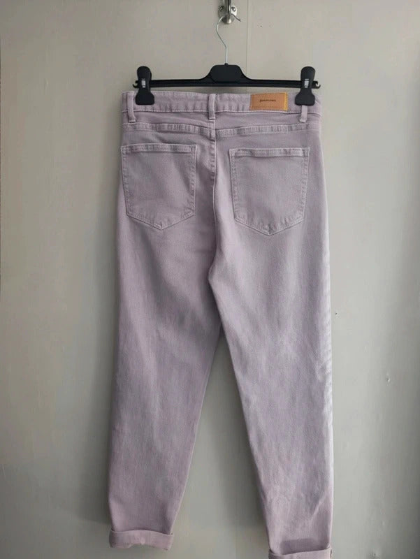 Light purple denim jeans shown from the back, hanging on a black hanger against a plain light gray wall.