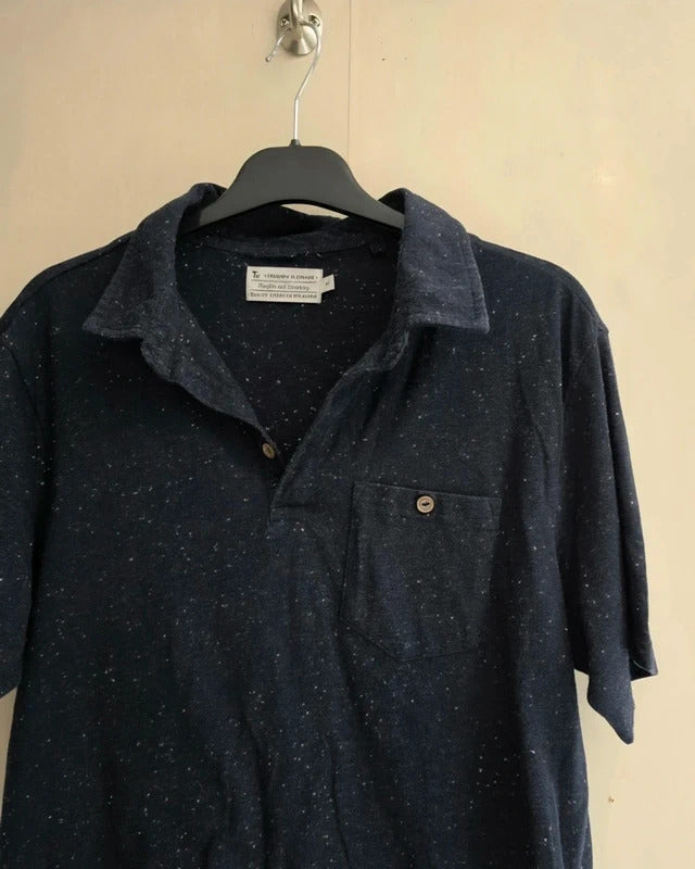 A dark navy blue short-sleeve button-up shirt with a subtle speckled pattern, hanging on a black hanger against a plain beige wall.