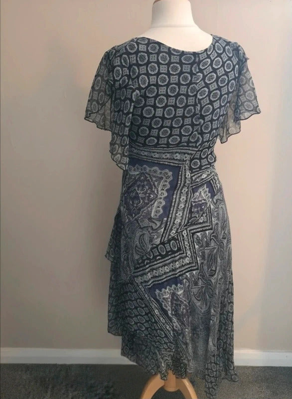 A short-sleeve midi dress with a mixed geometric and paisley print in navy blue and gray, displayed on a mannequin torso against a plain beige wall.