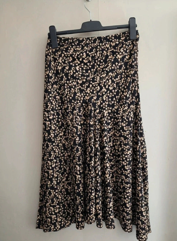 A black midi skirt with a beige and white floral print, hanging on a black hanger against a plain off-white wall.