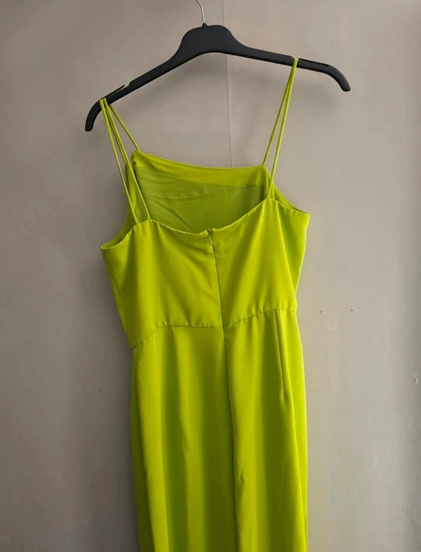 A bright lime green spaghetti-strap dress hanging on a black hanger against a plain beige wall.