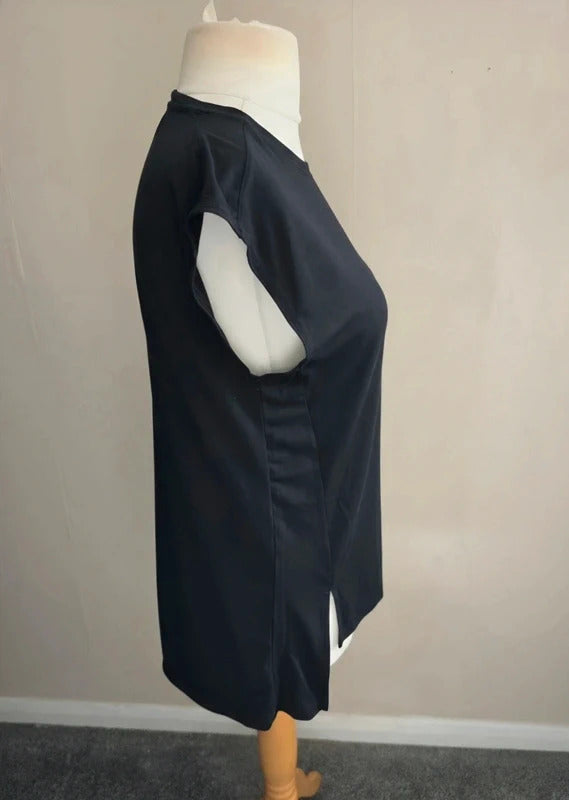 A black sleeveless tunic dress displayed on a white mannequin torso, shown from a side profile view against a plain beige wall.