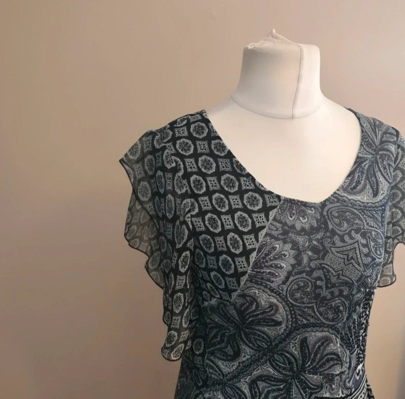 A sheer black and gray patterned dress 
displayed on a white mannequin torso against a plain beige wall.
