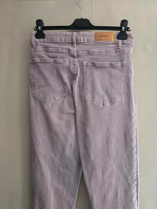 Light purple jeans shown from the back, hanging on a black hanger against a plain beige wall.