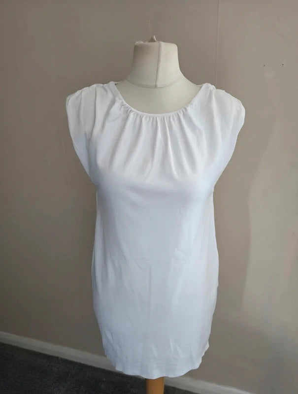 A white short-sleeve dress with a gathered, elasticized neckline, displayed on a cream dress form mannequin against a plain beige wall.