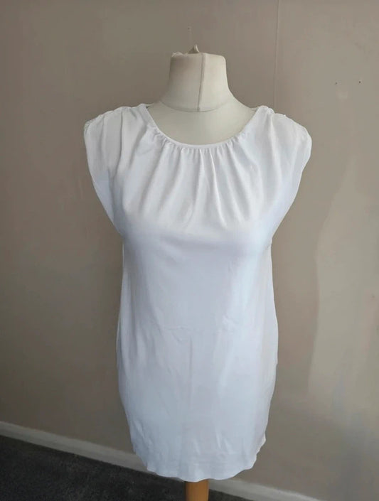 A white short-sleeve dress with a gathered, elasticized neckline, displayed on a cream dress form mannequin against a plain beige wall.