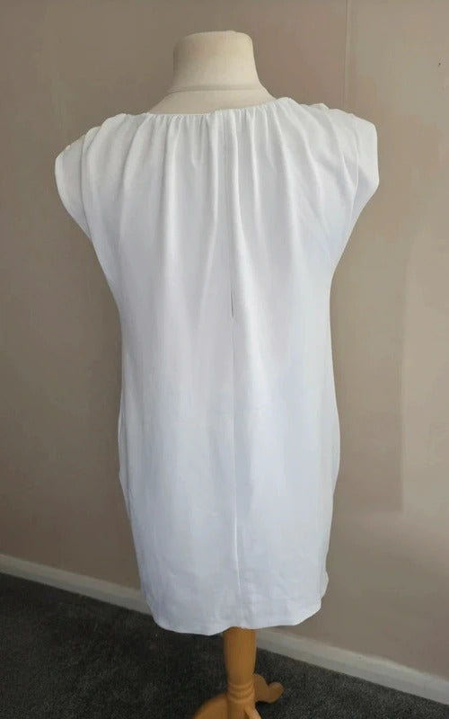 A white short-sleeve dress displayed on a mannequin torso, photographed indoors against a plain beige wall with dark carpet visible at the bottom.
