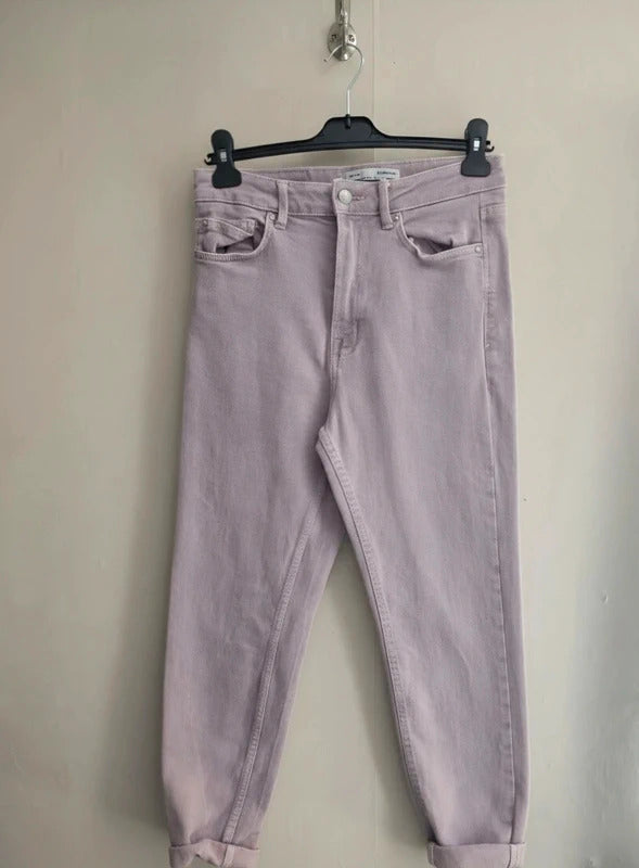Light purple denim jeans hanging on a black hanger against a plain beige wall.