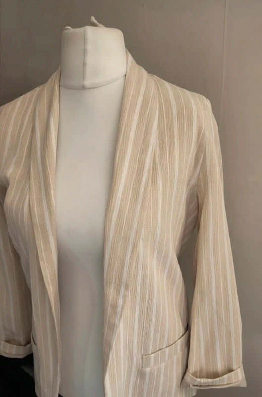 A cream and beige vertically striped open-front blazer jacket displayed on a white mannequin torso against a neutral gray background.