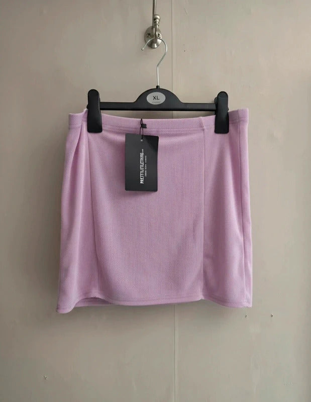 A light pink knit mini skirt hanging on a black hanger with a black hangtag, set against a plain beige wall.