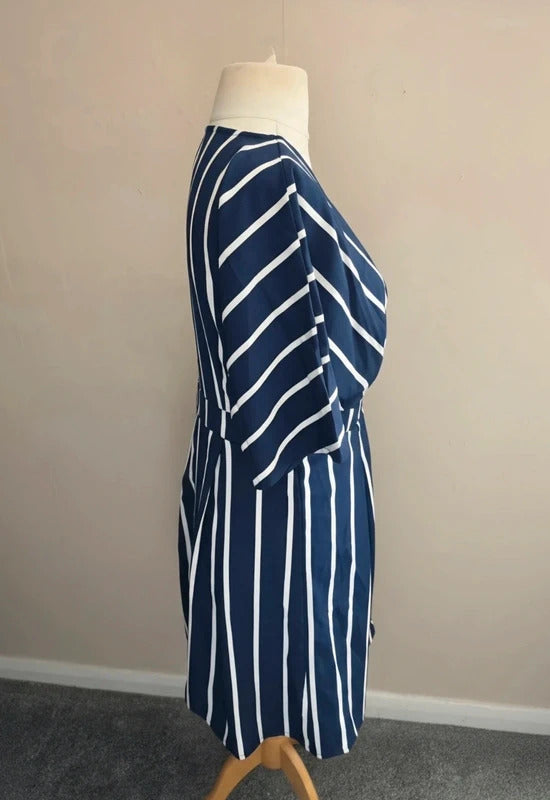 A navy blue and white vertically striped dress displayed on a mannequin torso in an indoor setting with a beige wall and gray carpet.