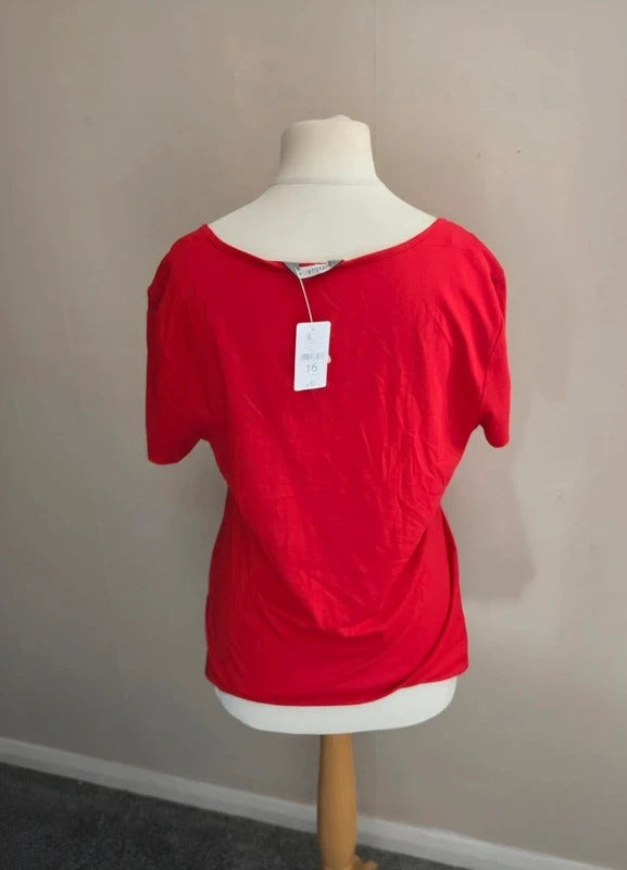 A bright red short-sleeve top displayed on a cream dress form mannequin against a plain beige wall.