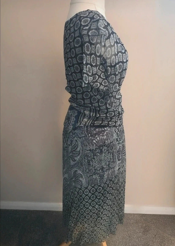 A long-sleeve maxi dress with a dark gray and white paisley pattern, displayed on a mannequin in a side profile view against a plain beige wall.