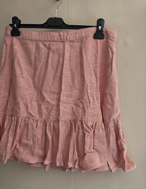 A pink ruffled mini skirt made of a textured linen-like fabric, hanging from a black hanger against a plain beige wall.