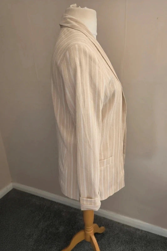 A cream-colored pinstripe blazer displayed on a mannequin torso with a wooden stand against a plain indoor wall.