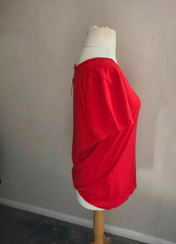 A bright red draped short-sleeve top displayed on a white dress form mannequin against a plain gray wall.