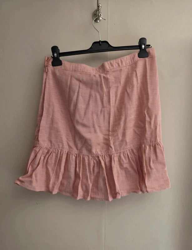 A dusty pink linen ruffled mini skirt hanging from a black plastic hanger against a plain beige wall.