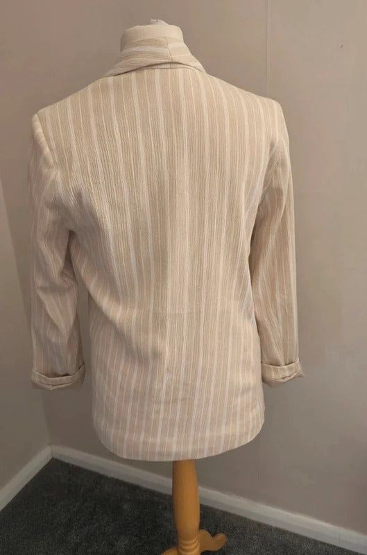 A cream and beige vertically striped linen-blend blazer displayed on a wooden dress form mannequin in a room corner.