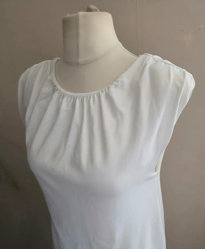 A white sleeveless dress with a gathered, pleated neckline, displayed on a cream-colored mannequin torso against a plain beige wall.