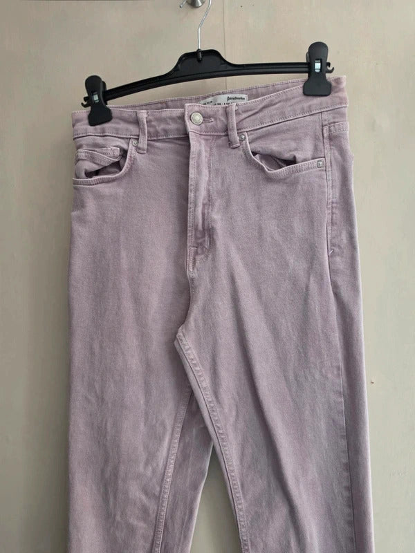 Lilac denim jeans hanging on a black hanger against a plain beige wall.
